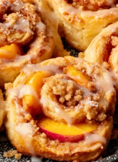 Peach Cobbler Cinnamon Rolls drizzled with icing on a wooden table