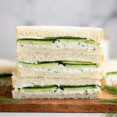 A fresh cucumber sandwich on a plate with herbs and a cup of tea.