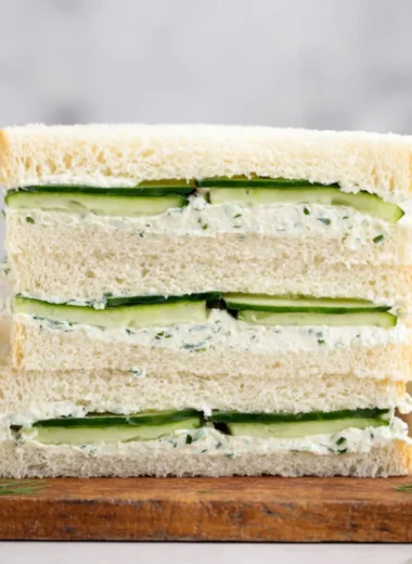 A fresh cucumber sandwich on a plate with herbs and a cup of tea.